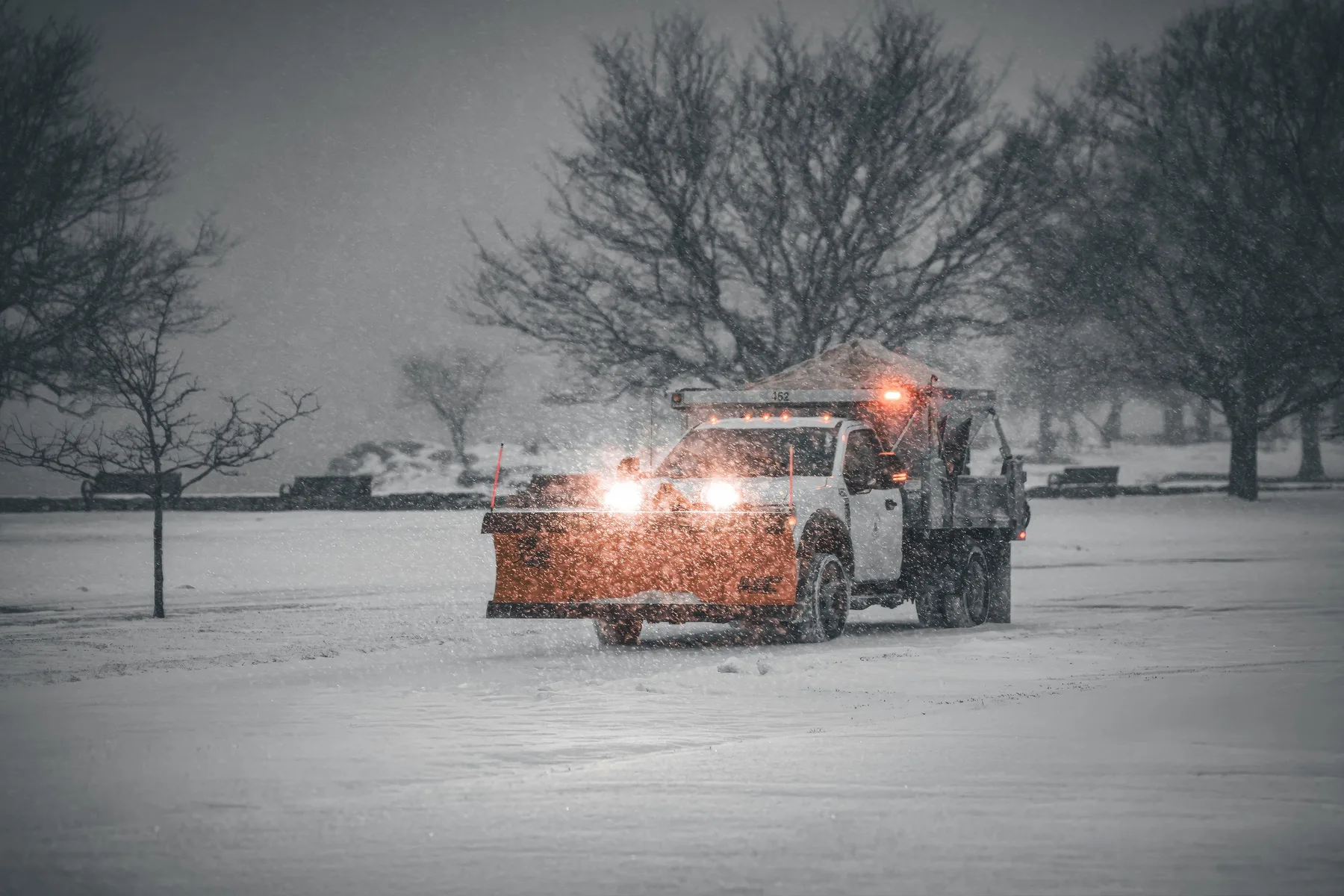 Snowplow truck clearing a snow-covered roadway during a storm